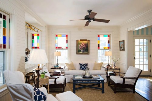 Bright living room with white furniture, colorful stained glass windows, and a ceiling fan, creating a cozy atmosphere.
