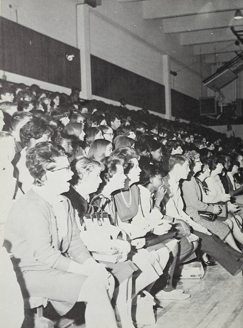 A large crowd of people seated in a gymnasium, mostly women, attending an event. The image is in black and white.