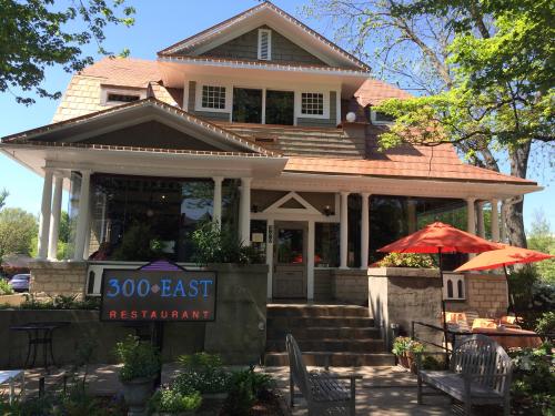 A charming restaurant with a large porch, surrounded by trees and outdoor seating, featuring a sign that reads "300 East."