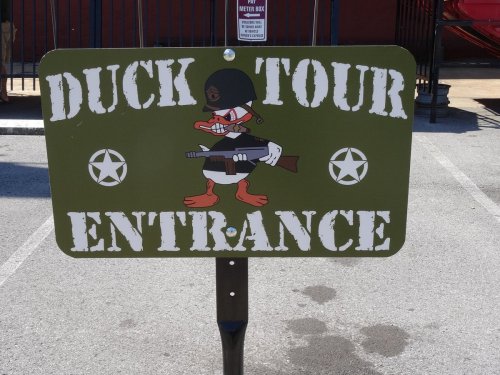 Sign for "Duck Tour Entrance" featuring a cartoon duck in military attire holding a rifle, with stars on either side.