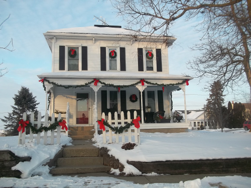 A festive house decorated with wreaths and bows, surrounded by snow and a white picket fence.