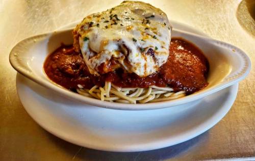 A dish of spaghetti topped with marinara sauce and a baked meatball covered in melted cheese.