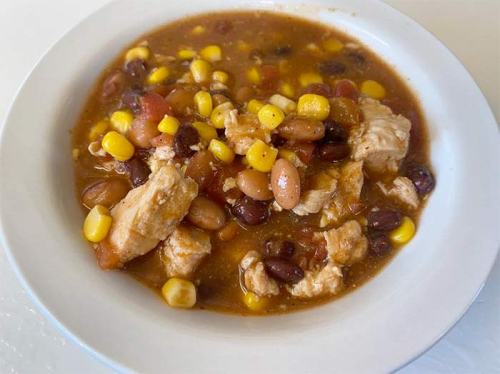 A bowl of hearty chicken chili with beans, corn, and diced tomatoes.