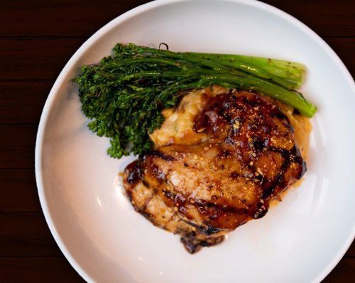 A plate featuring grilled chicken with a glossy glaze, served alongside sautéed broccolini.