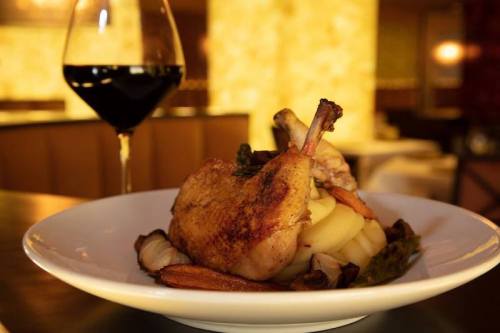 A plate of roasted chicken with mashed potatoes and vegetables, accompanied by a glass of red wine.