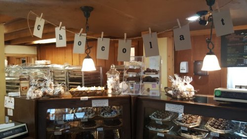 A cozy chocolate shop interior with a sign spelling "chocolat" and displays of various chocolates and treats.