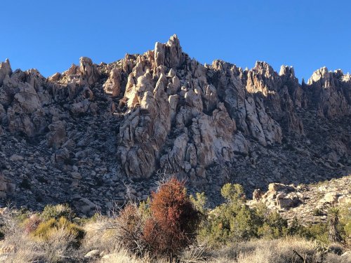 Rocky mountain landscape with jagged peaks under a clear blue sky, surrounded by sparse vegetation.