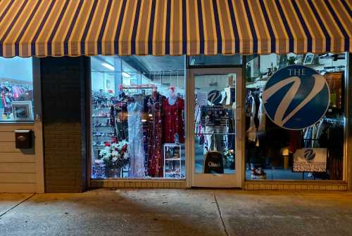 A storefront at night featuring a variety of clothing and accessories, with a large sign reading "The V."