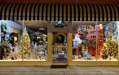 A festive storefront decorated with Christmas trees, lights, and holiday decor, featuring a red telephone booth.