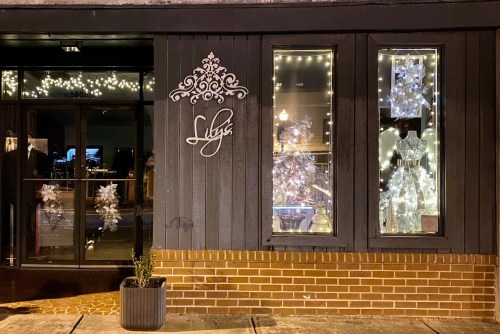 A storefront at night, decorated with white lights and festive displays in the windows. The sign reads "Lily's."