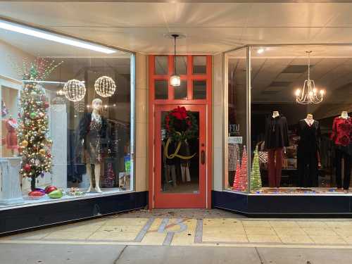 A festive storefront with holiday decorations, including a Christmas tree and elegant clothing displays.