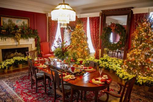 A festive dining room decorated for the holidays, featuring a beautifully set table, Christmas trees, and elegant decor.