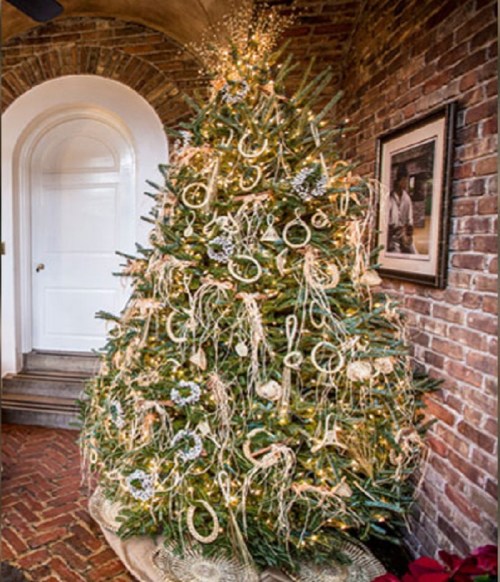 A beautifully decorated Christmas tree with lights and ornaments, set in a cozy brick-walled room.