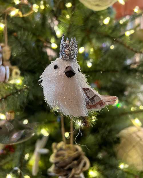 A fluffy white bird ornament with a silver crown, hanging on a decorated Christmas tree.