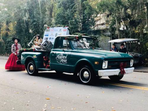 A decorated green pickup truck in a parade, with festive decorations and people in costumes nearby.