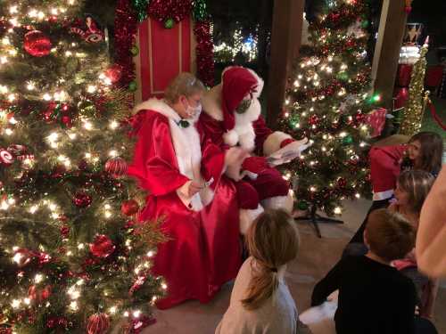 Santa and Mrs. Claus sit together, reading to children in a festive setting with Christmas trees and decorations.