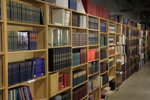 A wooden bookshelf filled with various books in different colors and sizes, arranged neatly in rows.