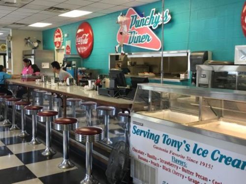 A retro diner interior with a counter, stools, and a menu featuring ice cream flavors and vintage decor.