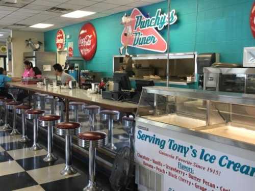 A retro diner interior with a counter, stools, and a menu featuring ice cream flavors and vintage decor.