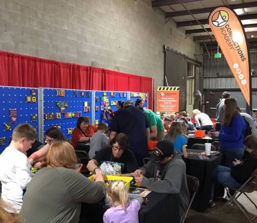 A busy indoor event with families and children engaged in hands-on activities at tables, surrounded by colorful displays.