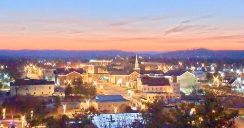 A scenic view of a town at sunset, with buildings and a church illuminated by streetlights against a colorful sky.