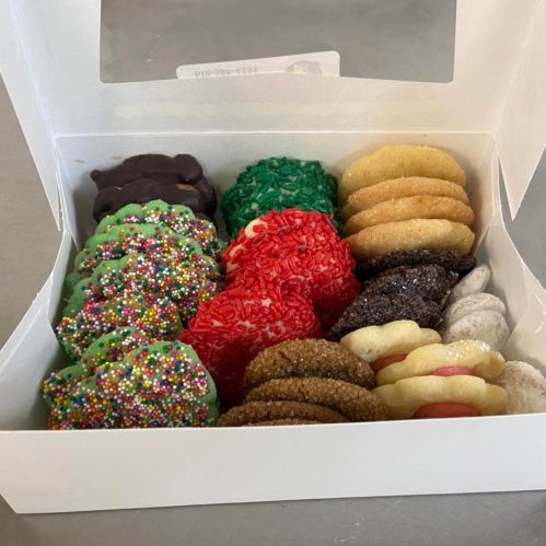 A white box filled with an assortment of colorful cookies, including sprinkles, chocolate, and festive decorations.
