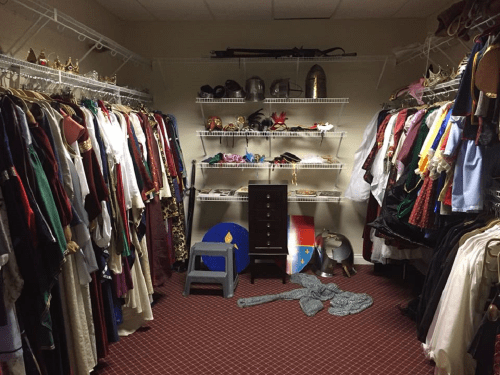 A cluttered costume closet filled with various outfits, accessories, and props on shelves and hanging racks.