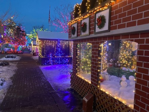 A festive street scene with decorated buildings, colorful lights, and snow, creating a cozy holiday atmosphere.