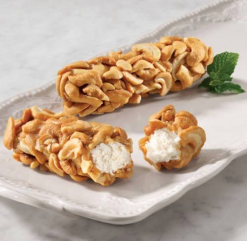 Two cashew-covered sweets on a decorative plate, one whole and one cut in half, revealing a creamy filling.