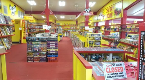 A colorful store interior filled with shelves of fireworks and snacks, featuring bright yellow and red decor.