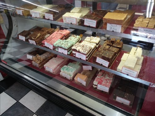 A display case filled with various colorful fudge squares, labeled with flavors, on a checkered floor.