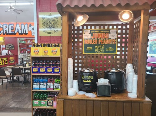 A wooden stand with signs for jumbo boiled peanuts, surrounded by drinks and a colorful diner interior.