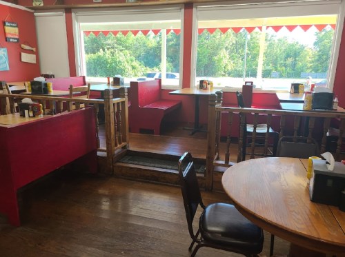 Cozy restaurant interior with wooden tables, red booths, and large windows overlooking greenery.