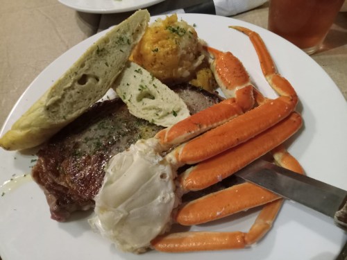 A plate featuring steak, crab legs, cornbread, and a side of seasoned potatoes.