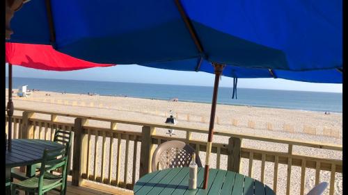 View of a beach with umbrellas, wooden deck, and people in the distance enjoying the sunny day by the ocean.