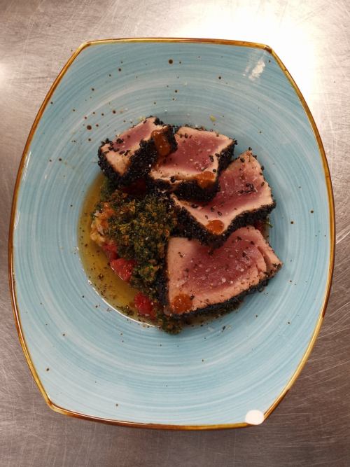 Seared tuna slices on a blue plate, garnished with a vibrant salsa and drizzled with sauce.