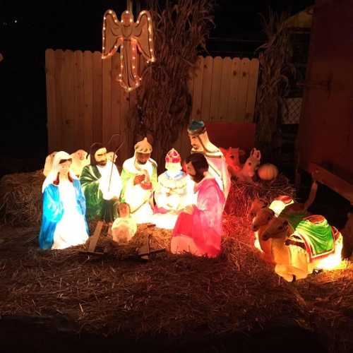 A colorful illuminated nativity scene with figures of Mary, Joseph, baby Jesus, and animals, set on hay.