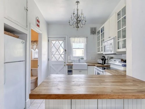 Bright kitchen with white cabinets, wooden countertop, chandelier, and a door leading outside. Cozy and inviting atmosphere.
