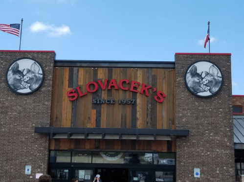 Exterior of Slovacek's store, featuring a wooden facade, red signage, and two circular images of boars.