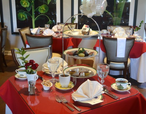 A beautifully set dining table with elegant dishes, tea cups, and a tiered stand of desserts in a cozy restaurant.
