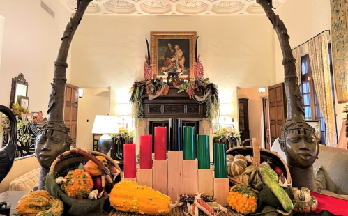 A festive display with decorative gourds, candles, and sculptures, set against a beautifully adorned fireplace.