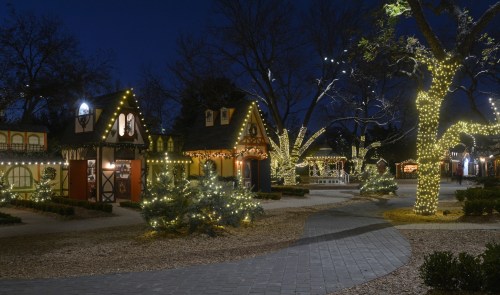 A festive scene of a park at night, featuring charming houses and trees adorned with twinkling holiday lights.