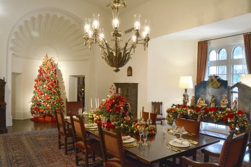 A festive dining room decorated for Christmas, featuring a large tree, elegant table settings, and holiday garlands.