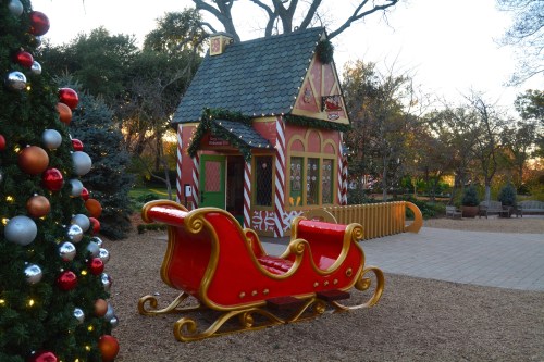 A festive scene featuring a red sleigh in front of a colorful holiday-themed house and a decorated Christmas tree.