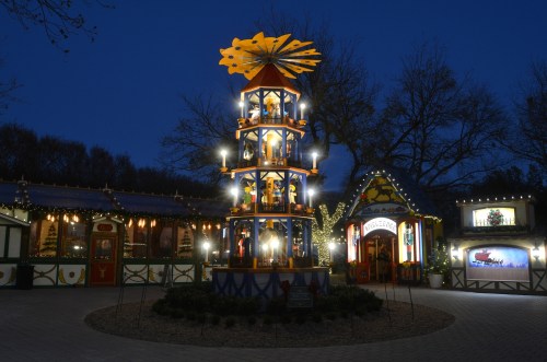 A brightly lit festive carousel with colorful decorations, surrounded by holiday lights in a nighttime setting.