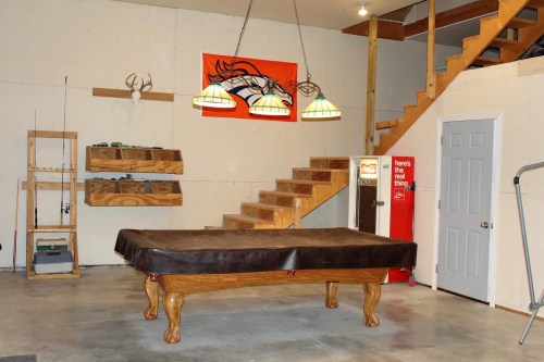 A garage with a pool table, wooden stairs, a Coca-Cola fridge, and a Denver Broncos banner on the wall.