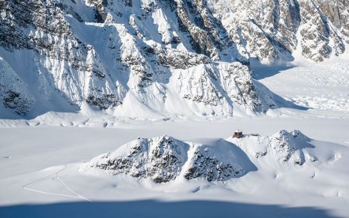 A snowy landscape with rugged mountains and a small cabin nestled among the snow-covered terrain.