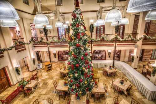 A tall Christmas tree adorned with ornaments stands in a festive dining area with tables and holiday decorations.