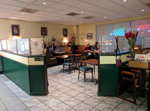 A cozy café interior with tables, chairs, and patrons dining, featuring a "For Sale" sign in the foreground.