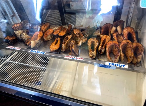 Display case with various smoked fish, including salmon and trout, labeled with their names.